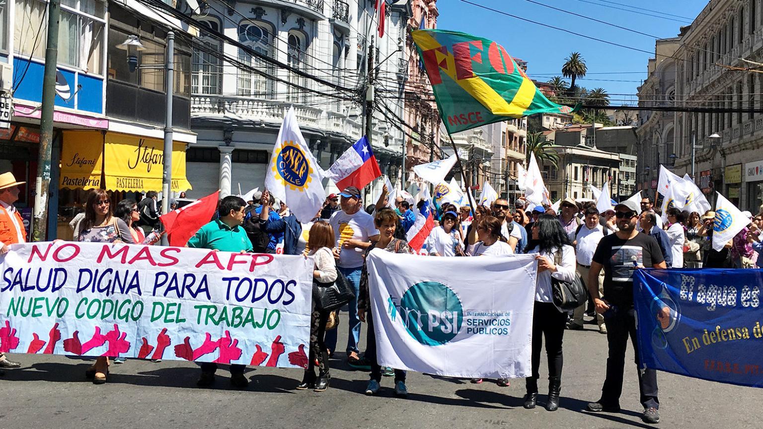 Syntolkning: Bild på människor i en demonstration i Chile. De håller i flaggor och går i led på gatan.